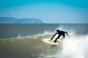 A surfer in a wetsuit carving a turn on a blue-grey ocean wave